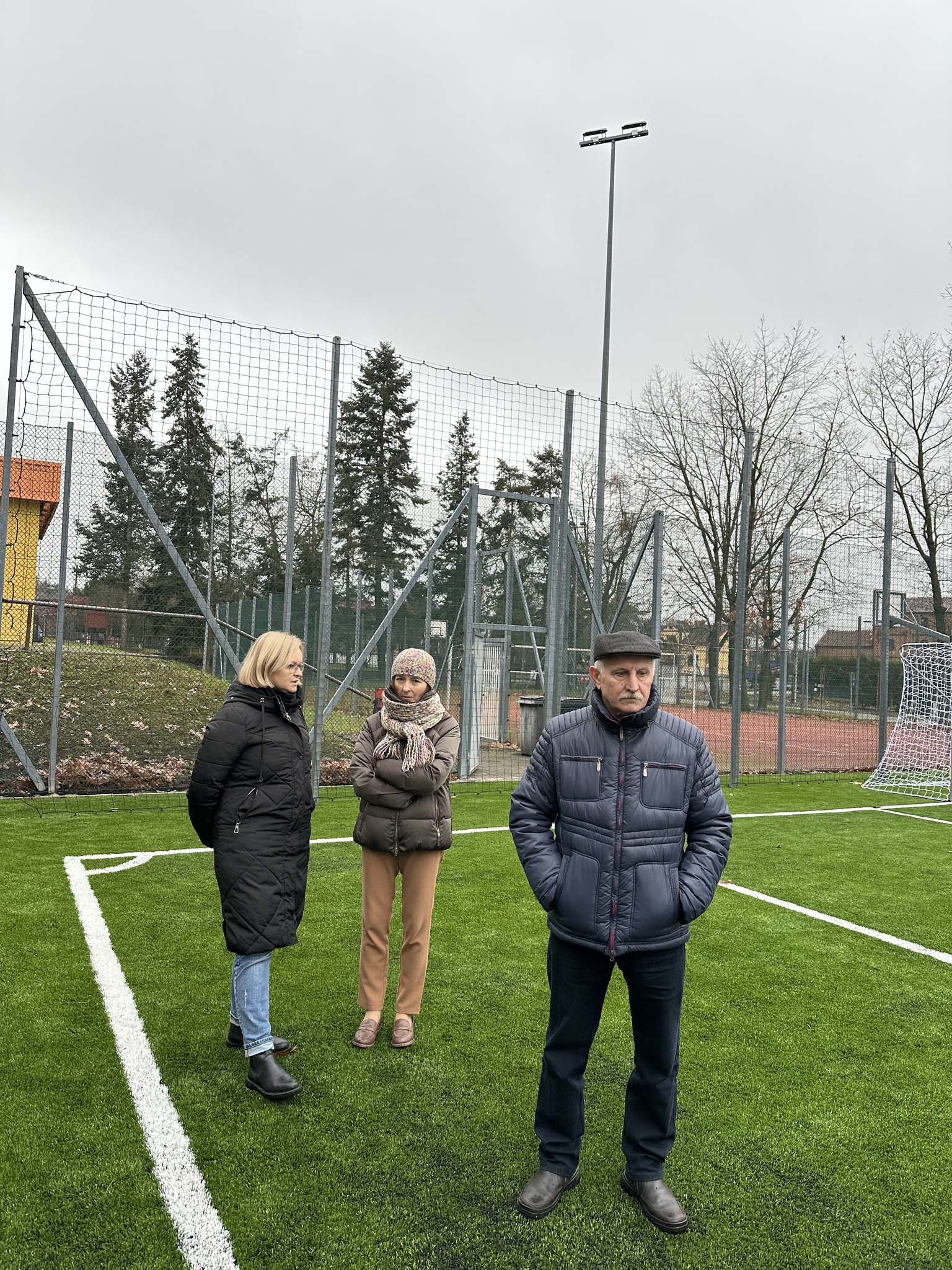 Trzy osoby idą po płycie boiska Orlik. Przedstawiciele urzędu oraz dyrektor szkoły